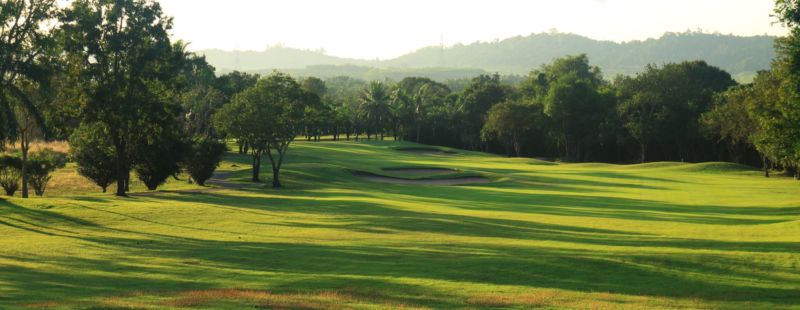 Fairway and bunkers in late-afternoon light, with wooded hills behind.