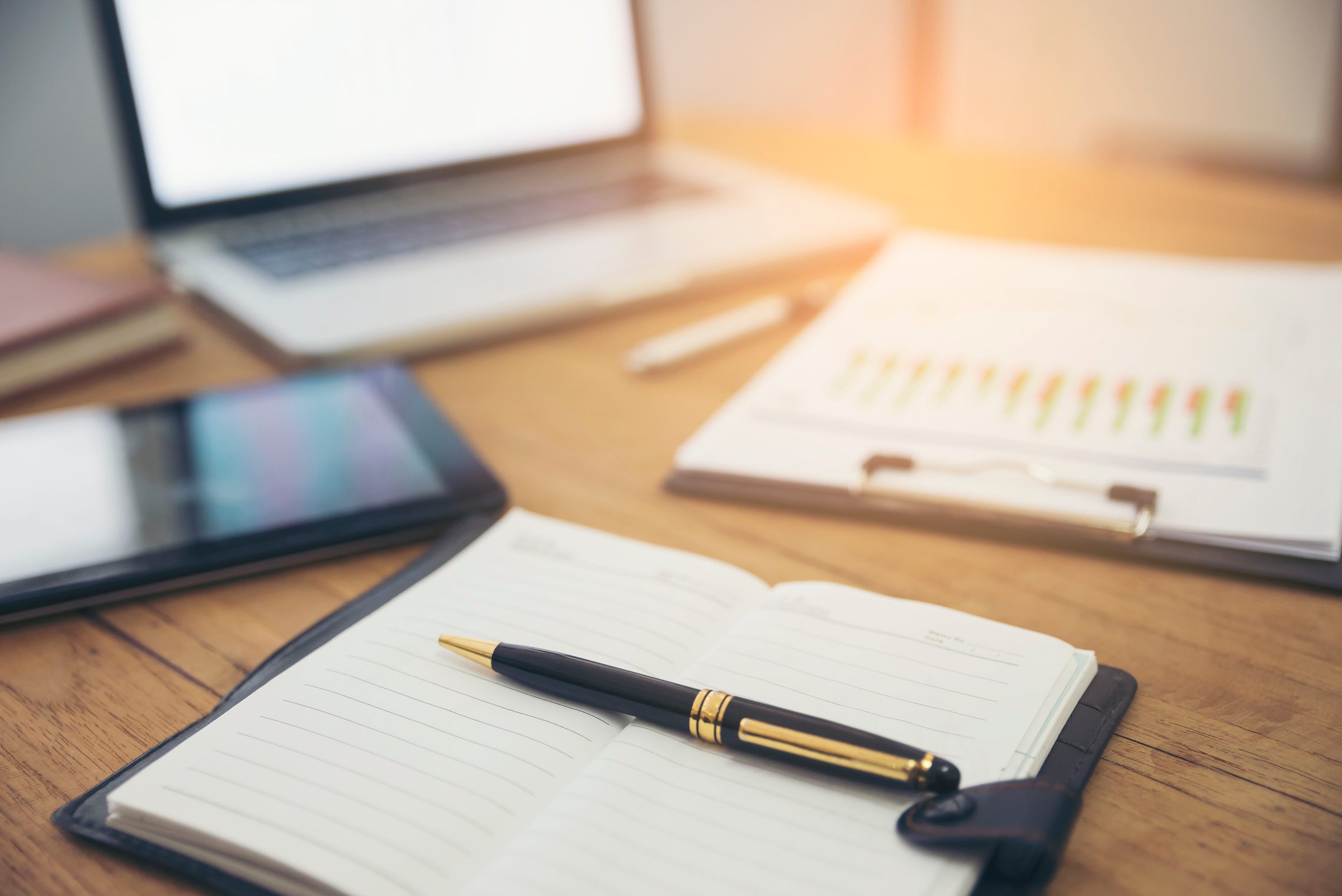 Notebook, pen and reports on a desk in warm light.